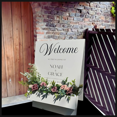 Welcome sign adorned with flowers, set against a rustic brick background.