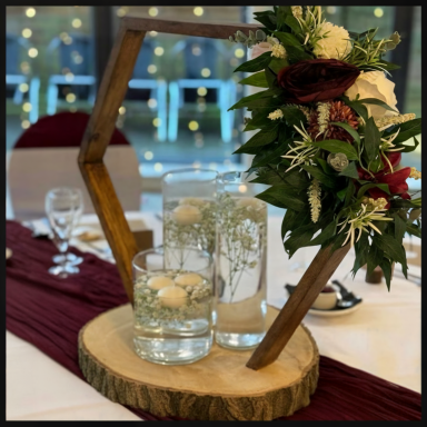 Decorative wooden stand with floral arrangement and glass vases on a table setting.