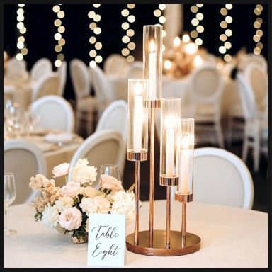 Elegant tall candle holders with flowers and a table number at a beautifully set dining table.