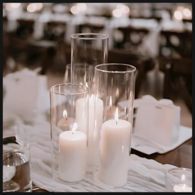 Group of glass candle holders with lit white candles on a table setting.