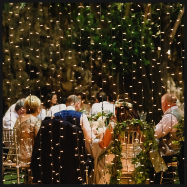 A group of people seated at a table, adorned with fairy lights and greenery.