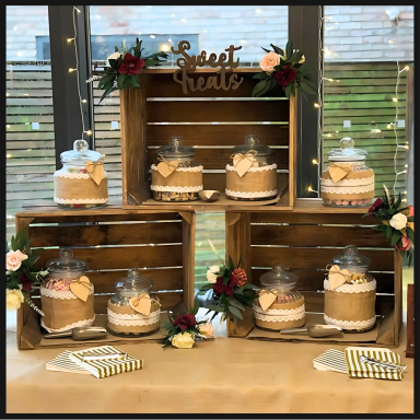 A display of decorated cakes in glass domes, arranged on wooden crates with floral accents.