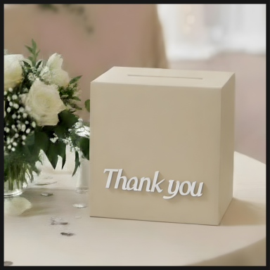 A beige donation box with "Thank you" written on the front, placed on a table.