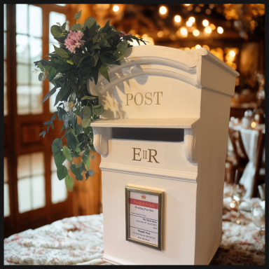 White postbox with ER insignia, adorned with a floral arrangement, in a vintage setting.