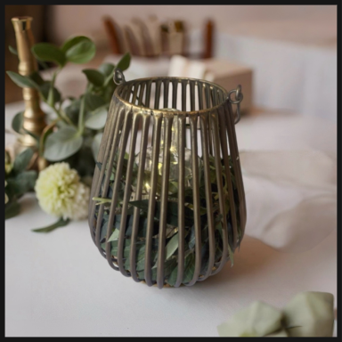 A decorative metal lantern with green foliage inside, placed on a table.