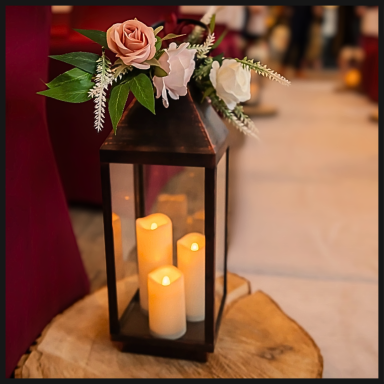 A decorative lantern with candles and flowers on a wooden surface.