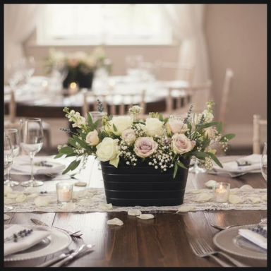 A floral arrangement in a black basket, set on an elegantly decorated dining table.