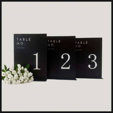 Three black table number cards with numbers 1, 2, and 3, alongside a bouquet of white flowers.