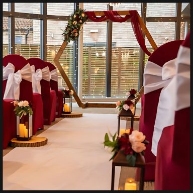 A decorated indoor wedding ceremony with red chairs and a floral arch.